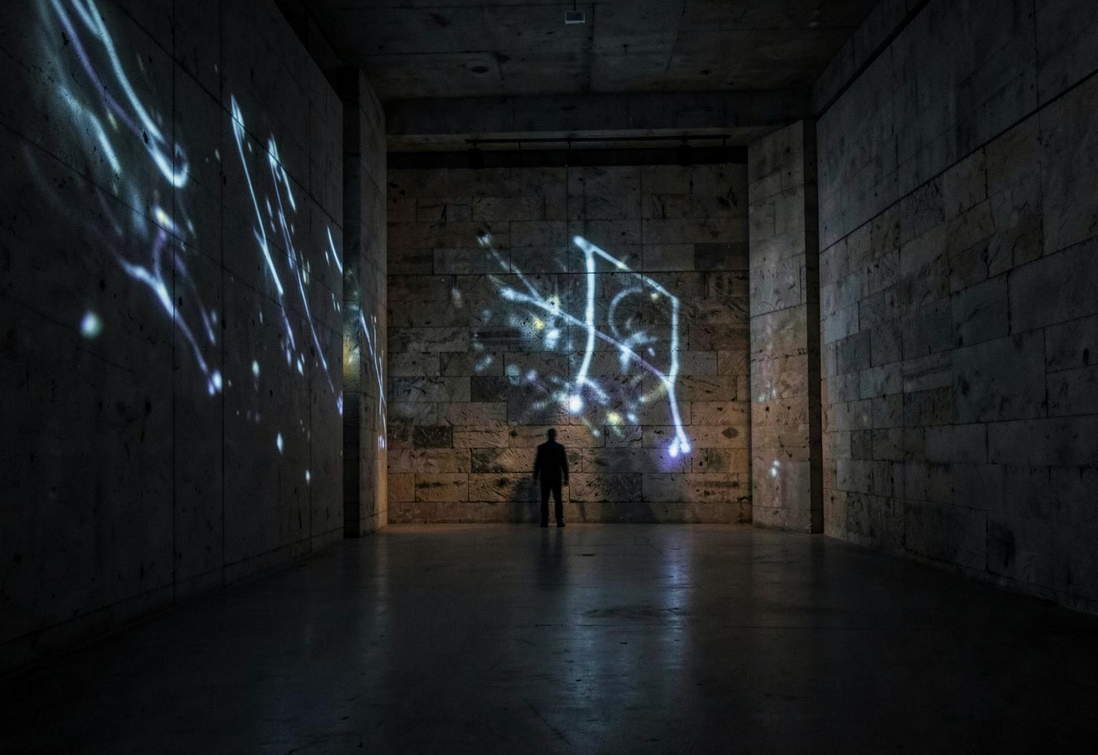 Projected light drawing across a stone gallery wall in a dark concrete space